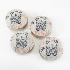 May include: Four round fabric buttons with a white background and a light pink and gray design. Each button features a cartoon koala wearing a striped shirt and the text "Sleepy Night" in pink.