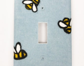 Puede incluir: Tapa de interruptor de luz azul claro con un patrón de abejas amarillas y negras.