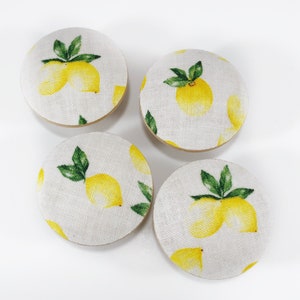 Peut inclure: Quatre boutons ronds recouverts de tissu avec un motif de citron. Les boutons sont blancs avec des citrons jaunes et des feuilles vertes.