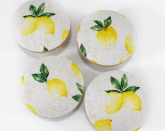 May include: Four round fabric covered buttons with a lemon print. The buttons are white with yellow lemons and green leaves.