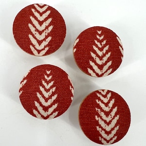 Op de afbeelding: Vier ronde, met stof beklede knoppen met een wit geometrisch patroon op een rode achtergrond.