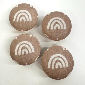 May include: Four brown fabric buttons with white rainbow designs. The buttons are round and have a textured surface.