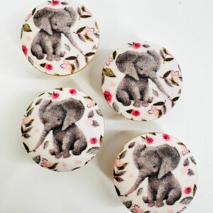 May include: Four round wooden knobs with a white fabric covering featuring a gray elephant with pink flowers and green leaves.