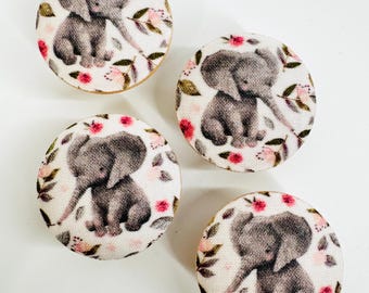 May include: Four round wooden knobs with a white fabric covering featuring a gray elephant with pink flowers and green leaves.
