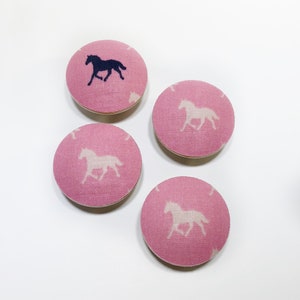 Może przedstawiać: Cztery różowe guziki z tkaniny z wzorem białej sylwetki konia. Guziki są okrągłe i mają białą sylwetkę konia w środku.