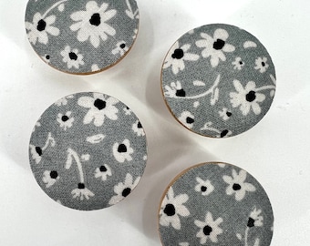 May include: Four round fabric covered buttons with a gray background and white floral pattern with black centers.