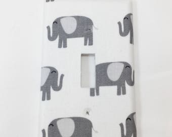 May include: White light switch cover with a gray elephant pattern. The elephants have a light gray body and a white ear.