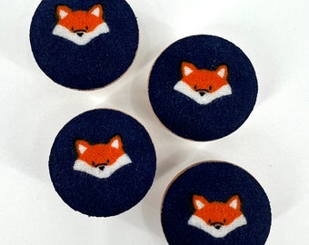 May include: Four round wooden buttons with a navy blue fabric covering. Each button features a white outline of a fox face with orange fur.