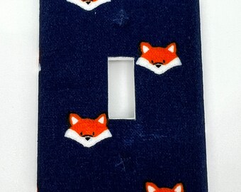 May include: A navy blue light switch cover with a repeating pattern of orange fox faces.
