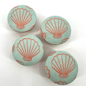 May include: Four round fabric covered buttons with a light blue background and a coral colored seashell design.