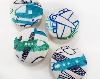 May include: Four round fabric buttons with a white background and blue, green, and black airplane and helicopter designs.