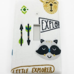 May include: White light switch cover with a woodland animal theme. The cover features a raccoon, a deer, arrows, and the text "Little Explorer".
