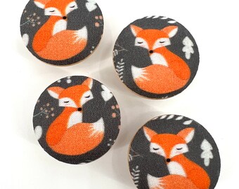 May include: Four round buttons with a black background and a white and orange fox design. The fox is curled up with its tail wrapped around its body. The buttons have a white and orange floral pattern around the fox.