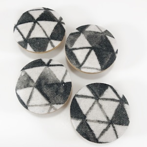 May include: Four round fabric covered buttons with a black and white geometric pattern. The pattern is made up of triangles.