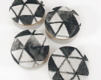 May include: Four round fabric covered buttons with a black and white geometric pattern. The pattern is made up of triangles.