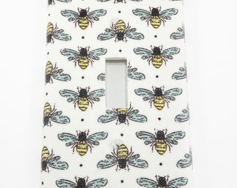 May include: White light switch cover with a repeating pattern of yellow and black bees on a light blue background.