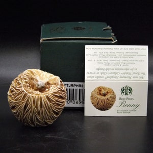 May include: A small, hand-painted ceramic figurine of a hedgehog curled up in a ball. The figurine is brown and white and has a detailed, realistic texture. The figurine is labeled "Roly Poly's Benny by Master Carver Adam Binder".