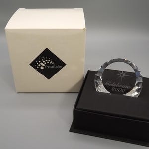 May include: A clear crystal arch with the text "Celebrate 2000" on a black base. A white box with a black diamond logo and the words "Crystal Colors" is to the left of the crystal arch.