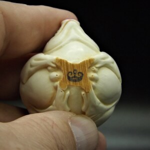 May include: A white ceramic figurine of a seated figure with a crown logo on a wooden base.