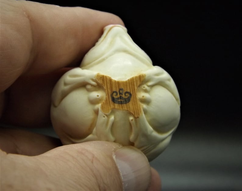 May include: A white ceramic figurine of a seated figure with a crown logo on a wooden base.