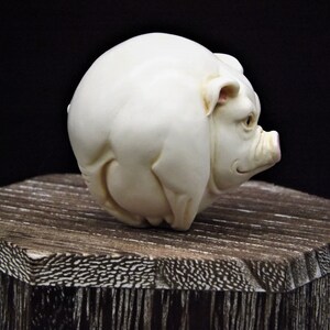 May include: A white ceramic sculpture of a pig. The pig is round and has a pink snout.