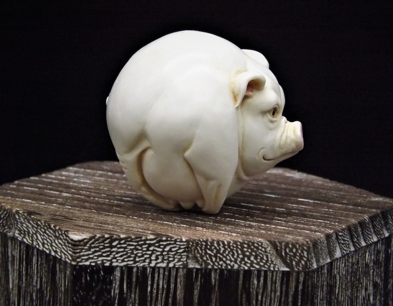 May include: A white ceramic sculpture of a pig. The pig is round and has a pink snout.
