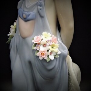 May include: A porcelain figurine of a girl wearing a blue dress with a bouquet of pink, yellow, and purple flowers tucked into the pocket.