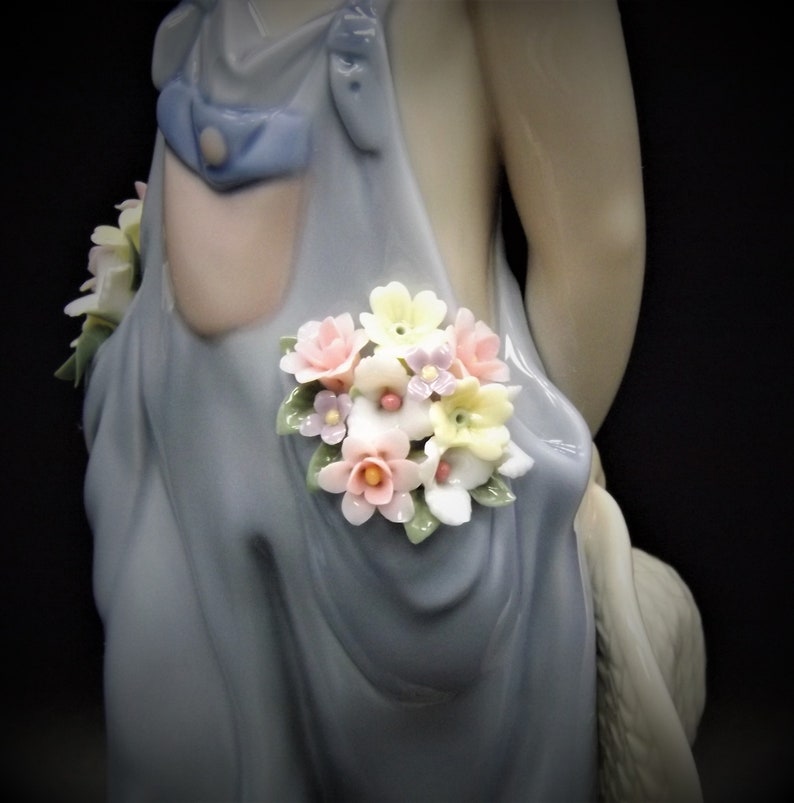 May include: A porcelain figurine of a girl wearing a blue dress with a bouquet of pink, yellow, and purple flowers tucked into the pocket.