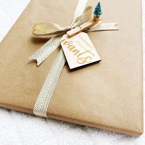 May include: A brown gift box wrapped with a gold ribbon and a wooden gift tag that says "Something Finley wants". A small green Christmas tree is attached to the tag with a wooden clothespin.