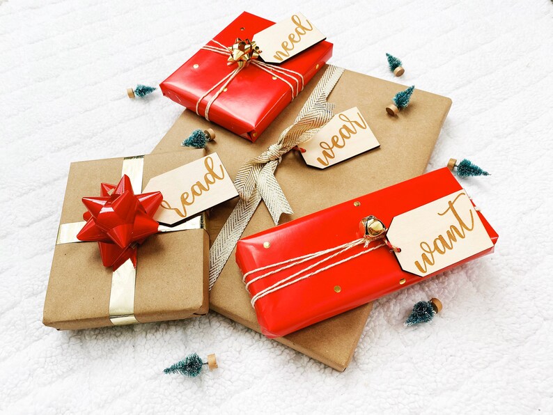 May include: Four wrapped gifts with red and brown paper, tied with twine and ribbon. Each gift has a wooden tag with gold lettering that says "need", "wear", "read", and "want".