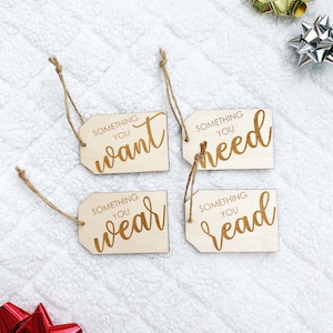 May include: Four wooden gift tags with twine attached. Each tag has the text "Something you" followed by a different word: "want", "need", "wear", and "read".