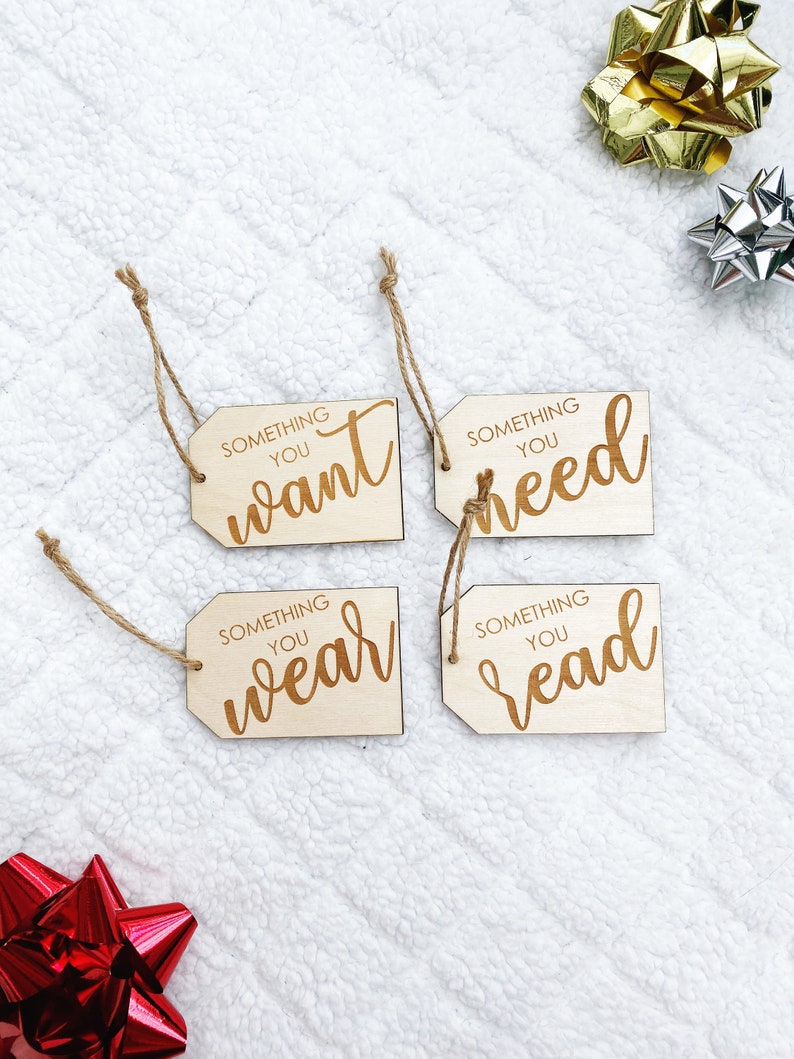 May include: Four wooden gift tags with twine attached. Each tag has the text "Something you" followed by a different word: "want", "need", "wear", and "read".