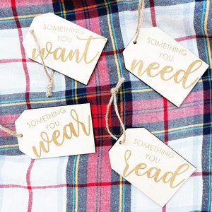 May include: Four wooden gift tags with twine attached. Each tag has a different phrase written on it: "Something you want", "Something you need", "Something you wear", and "Something you read".