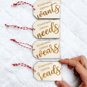 May include: Four wooden gift tags with red and white twine. The tags are engraved with the text "Something Griffin wants", "Something Griffin needs", "Something Griffin wears", and "Something Griffin reads".