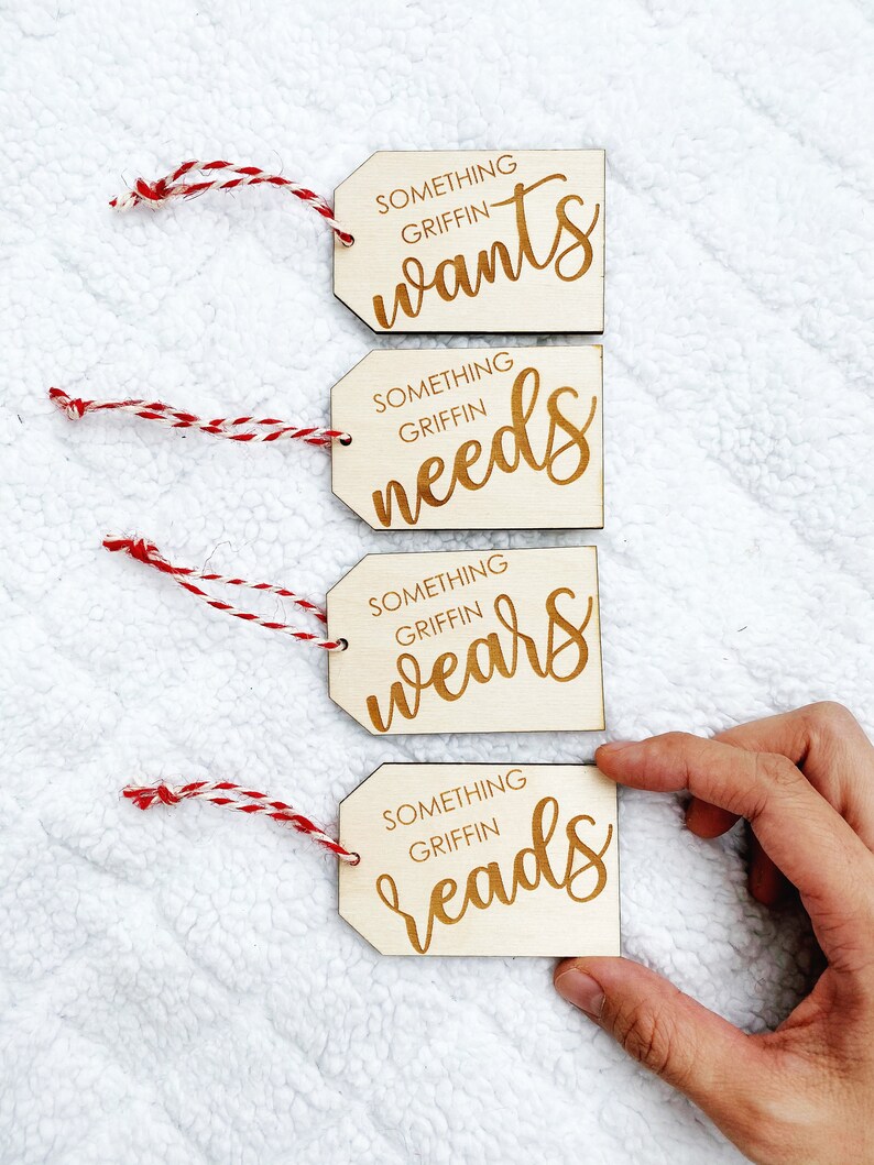 May include: Four wooden gift tags with red and white twine. The tags are engraved with the text "Something Griffin wants", "Something Griffin needs", "Something Griffin wears", and "Something Griffin reads".