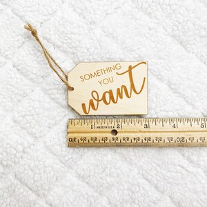 May include: A wooden tag with the text "SOMETHING YOU WANT" written in a cursive font. The tag is tied with a brown twine string.
