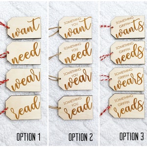 May include: Three sets of four wooden gift tags with red and white twine. Each set has the words "want", "need", "wear", and "read" with the text "Something you" or "Something Griffin" above the words.