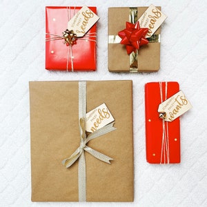 May include: Four wrapped gifts with brown paper and red ribbon. Each gift has a wooden tag with gold lettering. The tags read "Something Finley needs", "Something Finley wants", "Something Finley wears", and "Something Finley reads".