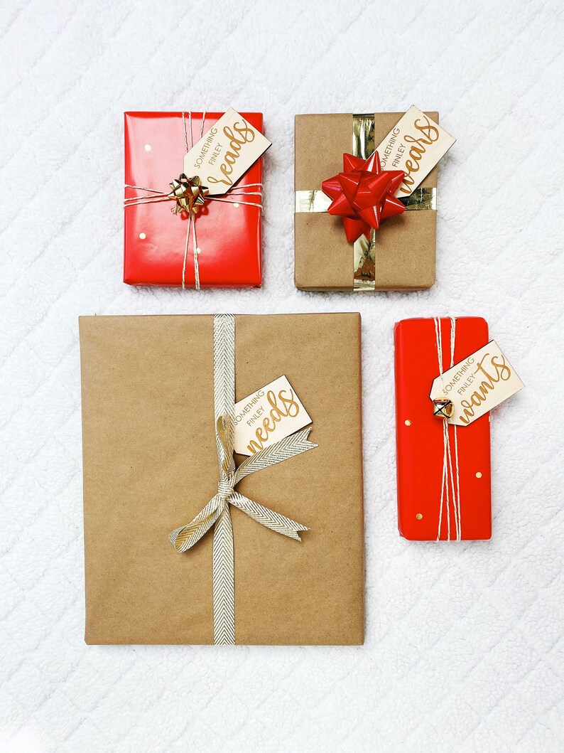 May include: Four wrapped gifts with brown paper and red ribbon. Each gift has a wooden tag with gold lettering. The tags read "Something Finley needs", "Something Finley wants", "Something Finley wears", and "Something Finley reads".
