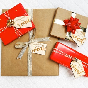May include: Four wrapped gifts with brown paper and red ribbon. Each gift has a wooden tag with gold lettering that says "Something you read", "Something you need", "Something you wear", and "Something you want".