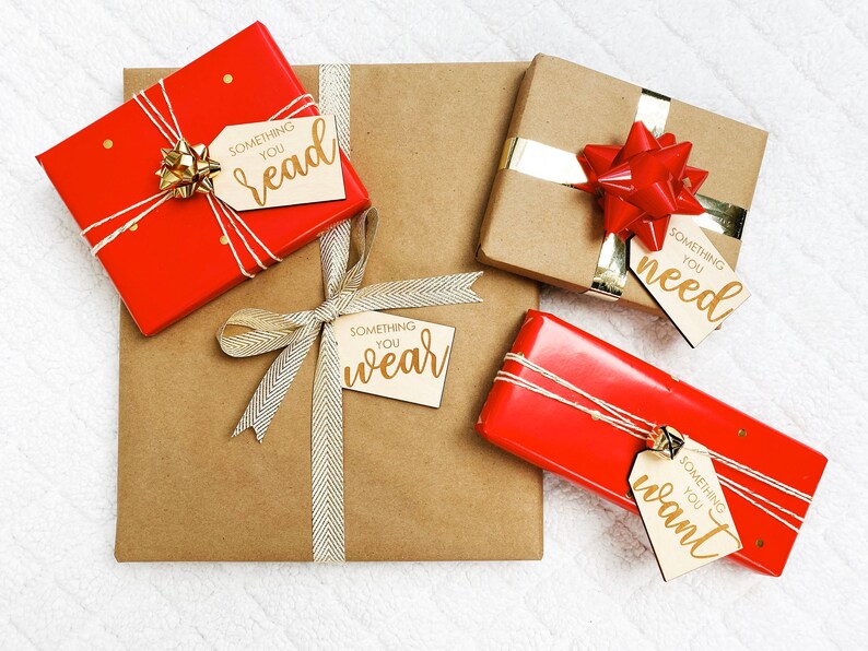 May include: Four wrapped gifts with brown paper and red ribbon. Each gift has a wooden tag with gold lettering that says "Something you read", "Something you need", "Something you wear", and "Something you want".