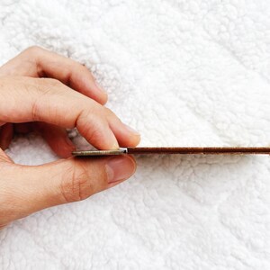 May include: A close-up of a wooden ruler being held by a hand. The ruler is brown and has a white edge. A coin is being used to hold the ruler in place.