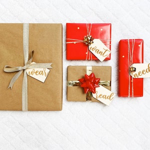 May include: Four wrapped gifts with gold ribbon and tags. The tags have the words "wear", "want", "read", and "need" written on them.