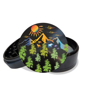 May include: A black metal grinder with a colorful mountain scene and sun on the lid. The scene includes green marijuana plants, clouds, and animals.