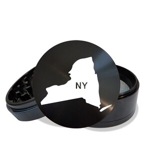 May include: Black metal grinder with a white outline of the state of New York and the letters "NY" inside the state. The grinder is open and the top is off.
