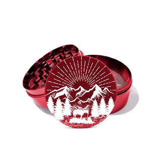 May include: Red metal grinder with a white mountain scene design. The design features a sun, mountains, trees, and a deer. The grinder is open, showing the grinding mechanism.