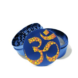 May include: A blue metal grinder with a circular design of the Om symbol in orange and yellow. The grinder is open, revealing the grinding mechanism and a screen.