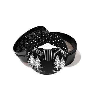 May include: Black metal grinder with a white design of a UFO flying over a mountain range with trees and stars in the night sky.