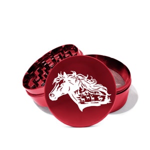May include: Red metal grinder with a white horse and deer design. The grinder has three parts, a top, a middle, and a bottom. The top has a horse's head with a forest scene in the background. The middle part has a grinder with teeth. The bottom part has a screen.