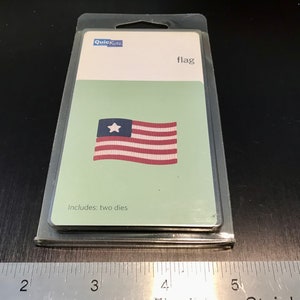 May include: A plastic package containing two metal dies for crafting. The dies are designed to cut out the shape of an American flag. The package is labeled "flag" and "Includes: two dies".